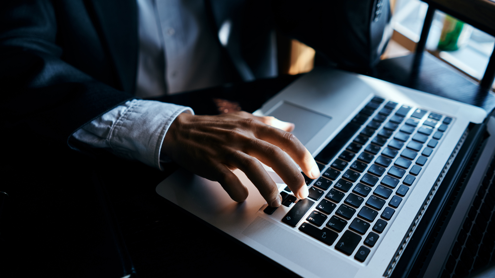 a person in a suit is typing on a laptop