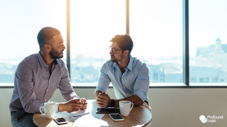 Two men discussing business in front of a large window.