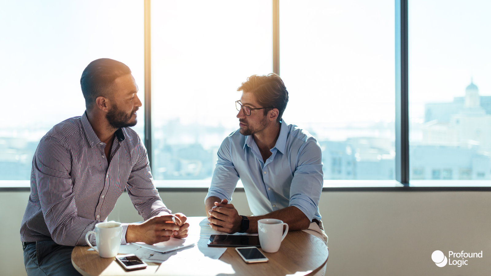 Two men discussing business in front of a large window.